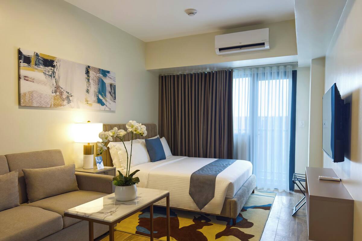 Una habitación de hotel con una cama, un sofá, un escritorio, un televisor y un cuadro en la pared.