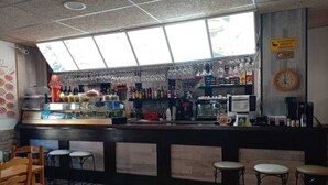 Zona de bar con taburetes, una barra con diversos artículos y una ventana arriba.