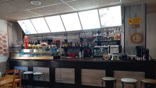 Zona de bar con taburetes, una barra con diversos artículos y una ventana arriba.