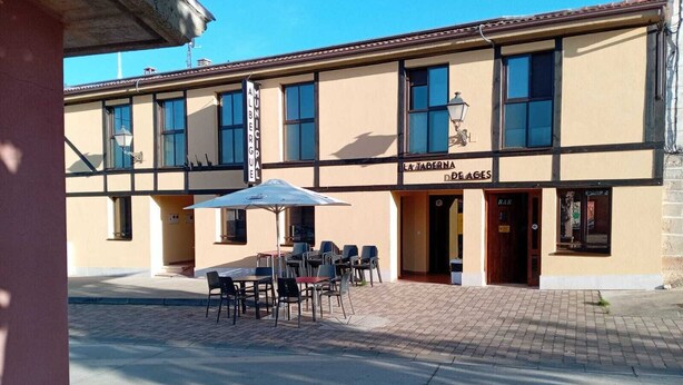 Un edificio con un letrero que dice "LA TABERNA D'AGES" y terraza con mesas y sillas.