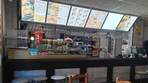 Un restaurante con un cartel de menú que muestra varios platos. Hay taburetes y una mesa en primer plano.