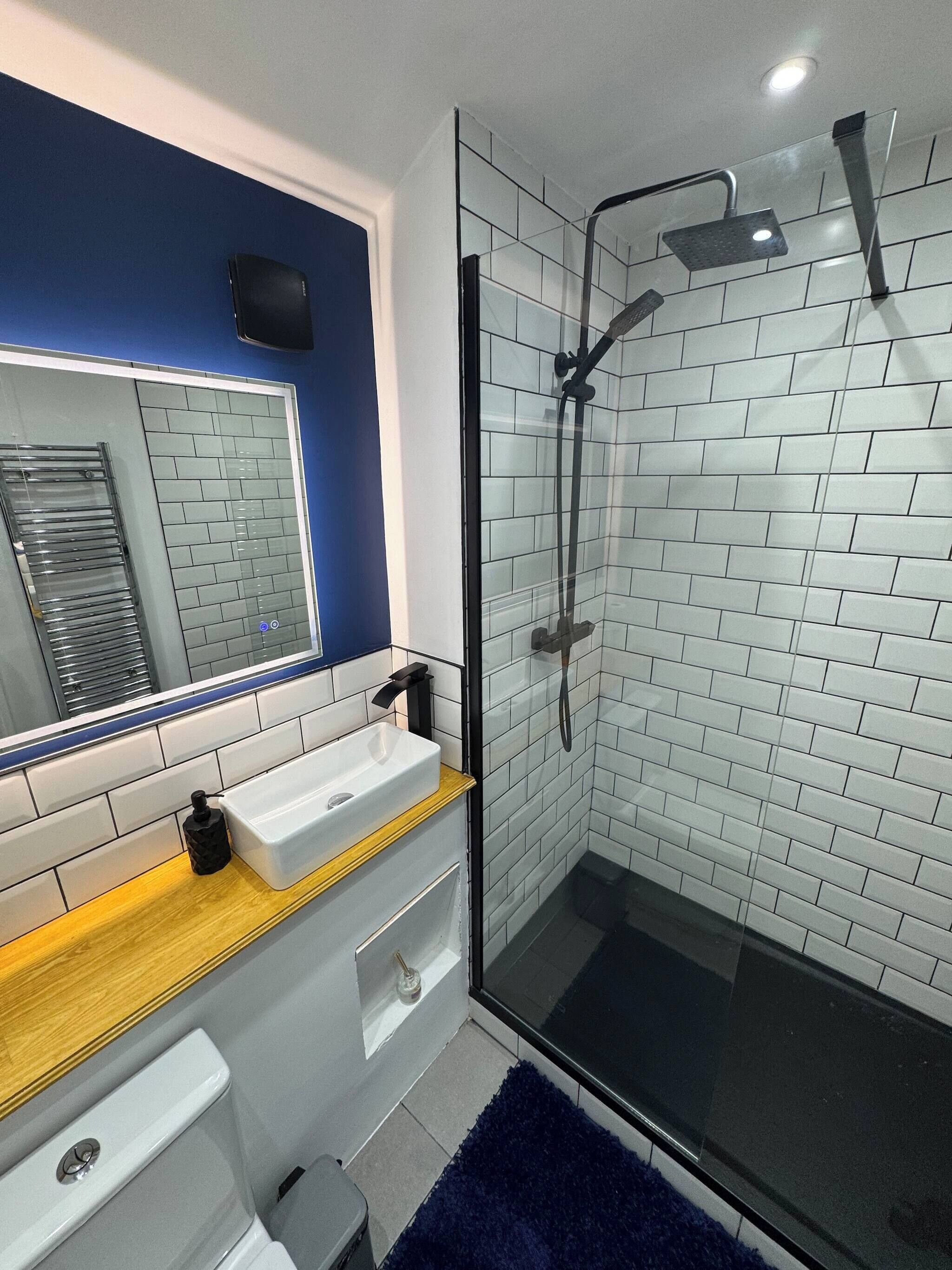 A modern bathroom with a glass-enclosed shower, white subway tiles, a wooden vanity, and a large mirror.