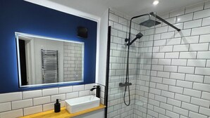 A modern bathroom with a glass-enclosed shower, a white sink with a wooden countertop, and a blue accent wall. - Tranquil Cambridge Getaway (Cambridge)