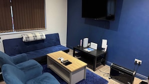 A modern living room with a blue sofa, a wooden coffee table, a TV mounted on the wall, and a heater on the floor. - Tranquil Cambridge Getaway (Cambridge)