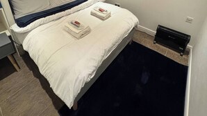 A modern bedroom with a bed, white bedding, a blue accent wall, and a small heater on the floor. - Tranquil Cambridge Getaway (Cambridge)
