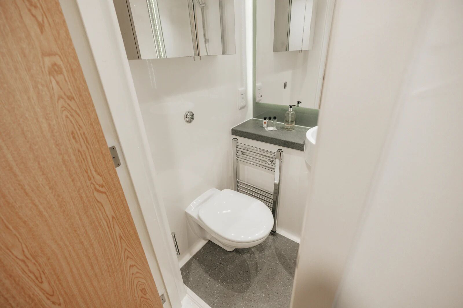 Ein kleines, sauberes Badezimmer mit Toilette, Waschbecken mit Seifenspender und Spiegel über dem Waschbecken.