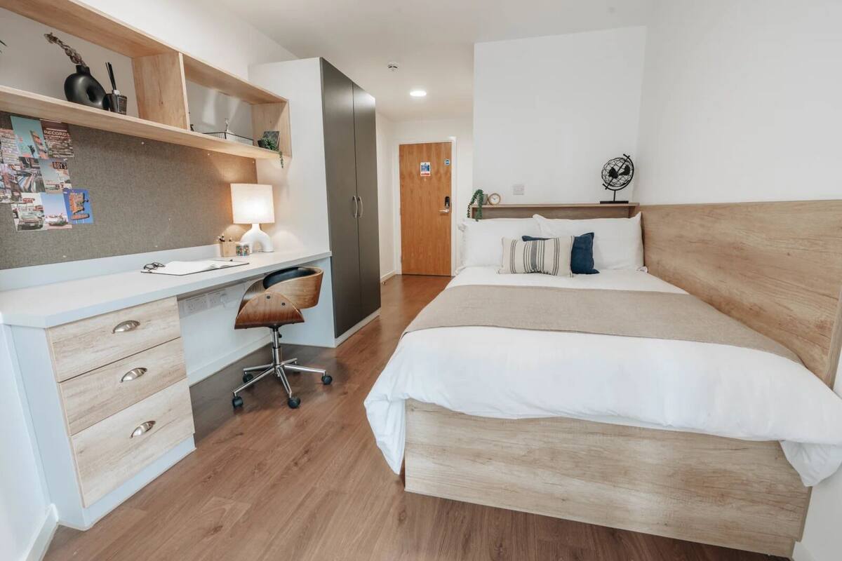 Ein modernes Schlafzimmer mit einem Holztisch, einem Stuhl, einem Bett mit Holz Kopfteil und einem kleinen Nachttisch mit einer Weltkugel.
