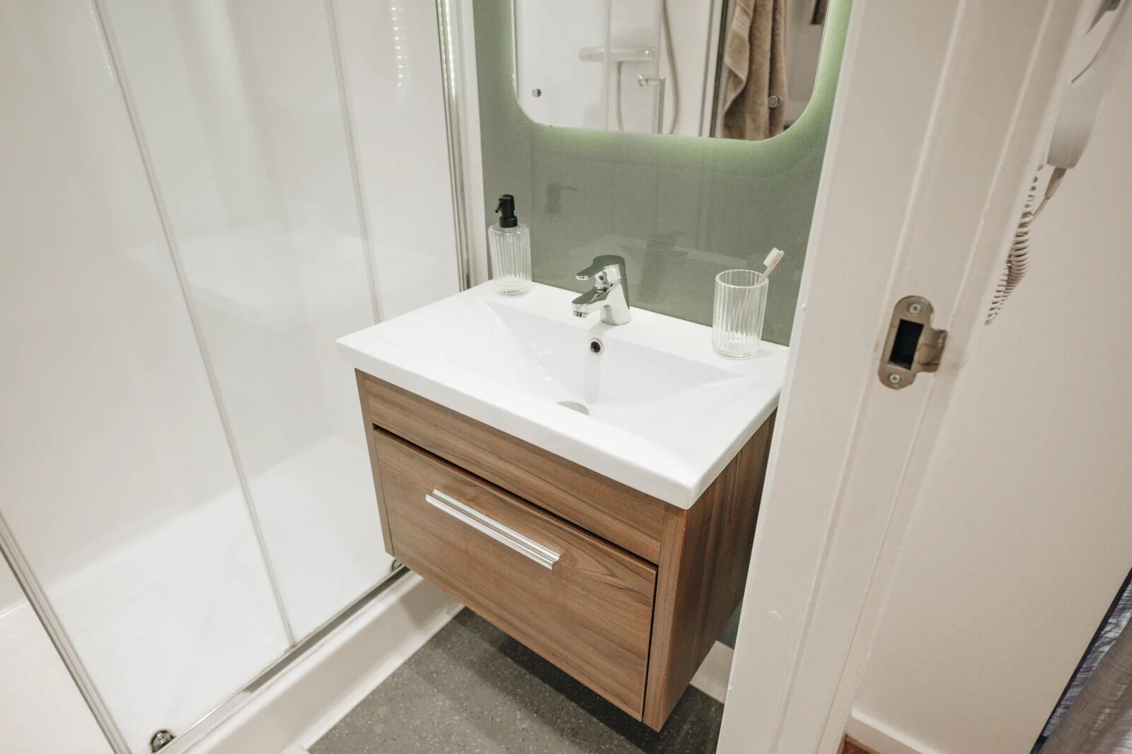 A bathroom with a white sink, wooden vanity, and a mirror with a green accent.