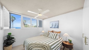 A bedroom with a bed, a ceiling fan, a window with blinds, a bedside table with a lamp, and a potted plant. - Oceanic Views at Kings Beach - 300m to the beach (Caloundra Region)