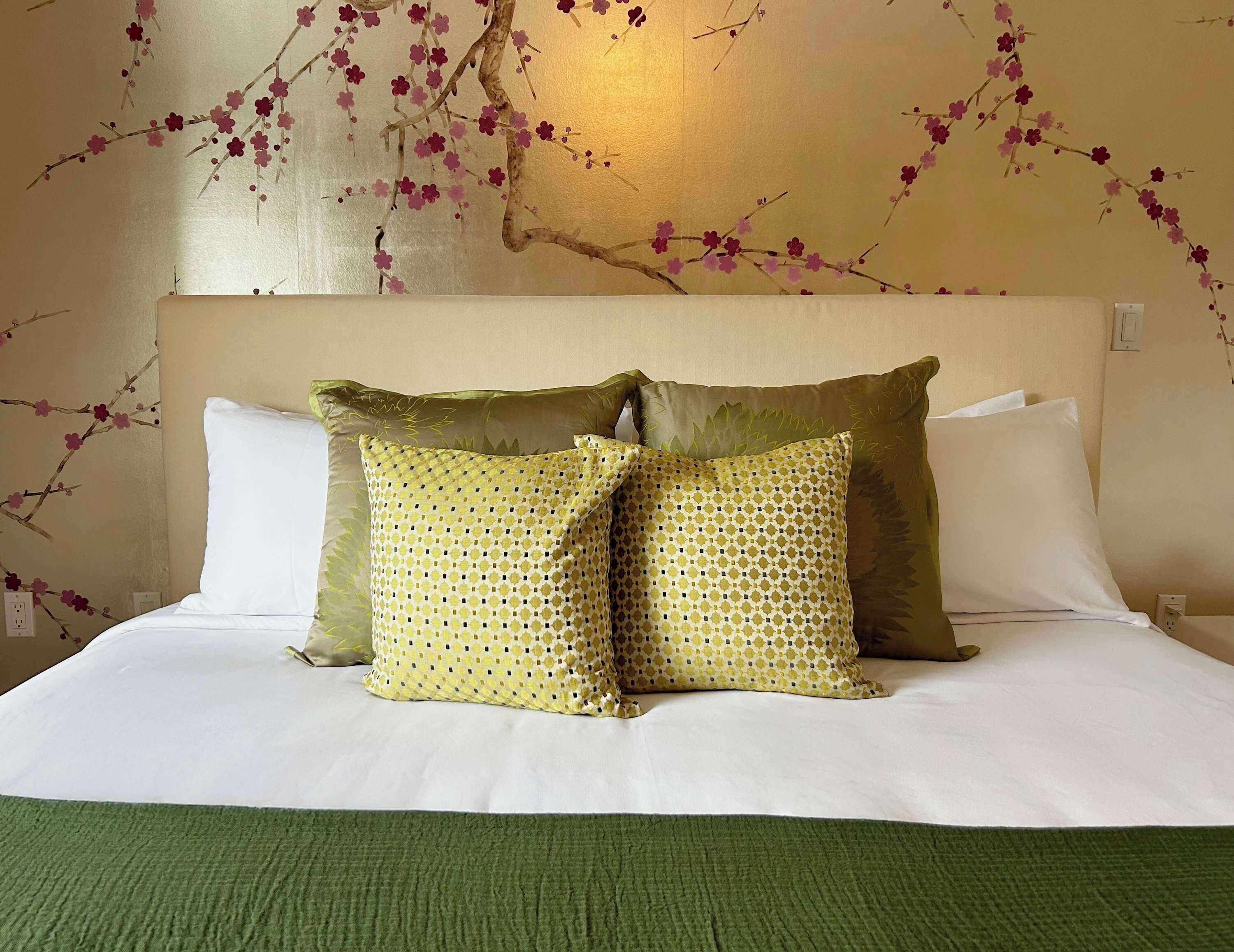 A neatly made bed with white linens, two patterned pillows, and a green throw blanket.