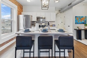 Uma cozinha moderna com armários brancos, uma ilha central com banquetas, eletrodomésticos de aço inoxidável e um mapa-múndi na parede.