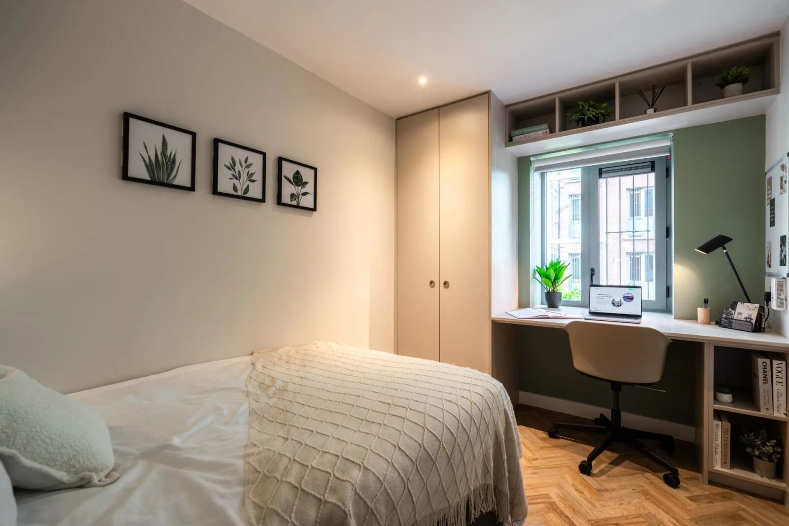 Un dormitorio con cama, escritorio y armario. Hay tres cuadros en la pared.