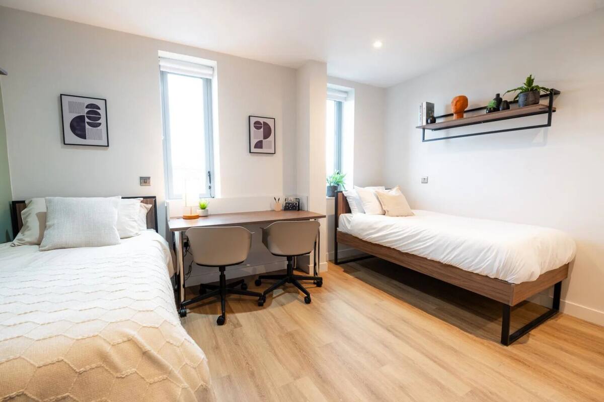 A compact bedroom with two beds, a desk, and two chairs.
