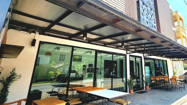 Ein Außenbereich mit Tischen und Stühlen, eine überdachte Terrasse und ein Gebäude mit großen Fenstern und einem Metalldach.