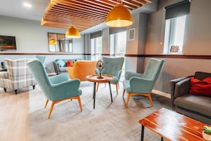 Un'area lounge moderna con poltrone color acquamarina, un tavolino in legno e un divano con cuscini rossi.
