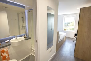 Un bagno moderno con lavandino, specchio e doccia. Nell'stanza adiacente, un letto con una finestra.