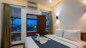Une chambre d’hôtel avec un lit, une fenêtre avec des rideaux, une vue sur des immeubles et un appareil de climatisation.