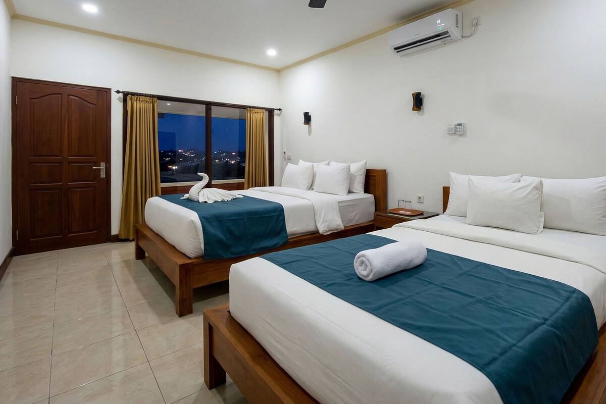 A hotel room with two beds, a view of the city at night, an air conditioning unit, and a telephone on the wall.