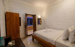 A bedroom with a wooden bed, white brick walls, a wooden door, and a small mirror. - Rumah Rini by Rumah Weda (Ubud)