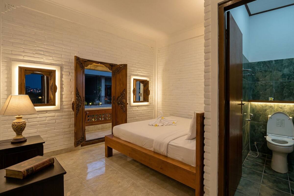 A bedroom with a wooden bed, a nightstand with a lamp, a mirror, and a view of the outside.