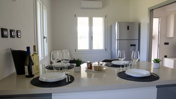 A modern kitchen with a large island, a refrigerator, and a dining area set for a meal. - VivimiHome - Monti House (Monti)