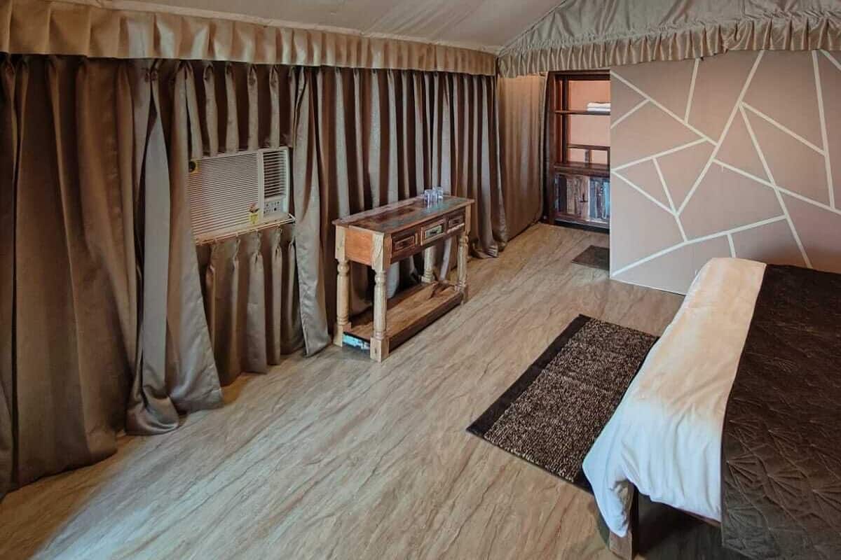 A spacious room with a high ceiling, a ceiling fan, a wooden console table, a bed with a white bedspread, and a geometric-patterned wall.