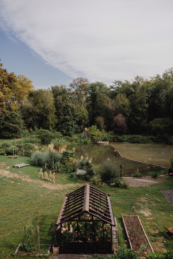 Een prieeltje in een tuin met een vijver en bomen op de achtergrond.