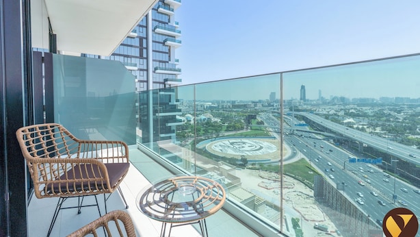 Ein Balkon mit Korbstühlen und einem Glastisch, mit Blick auf eine Stadtlandschaft aus modernen Gebäuden und einer Autobahn.