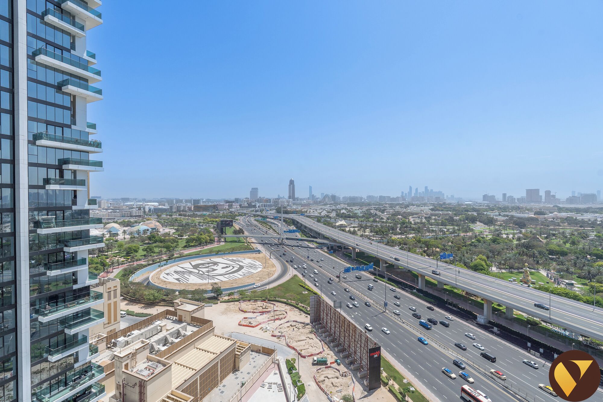 A high-rise building with multiple balconies and a view of a cityscape with highways and greenery.