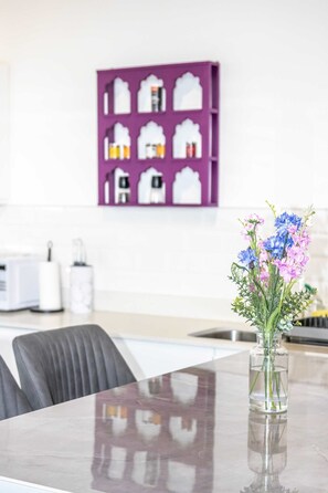 A modern kitchen with a purple wall art, a clear vase with flowers, and a stainless steel sink.