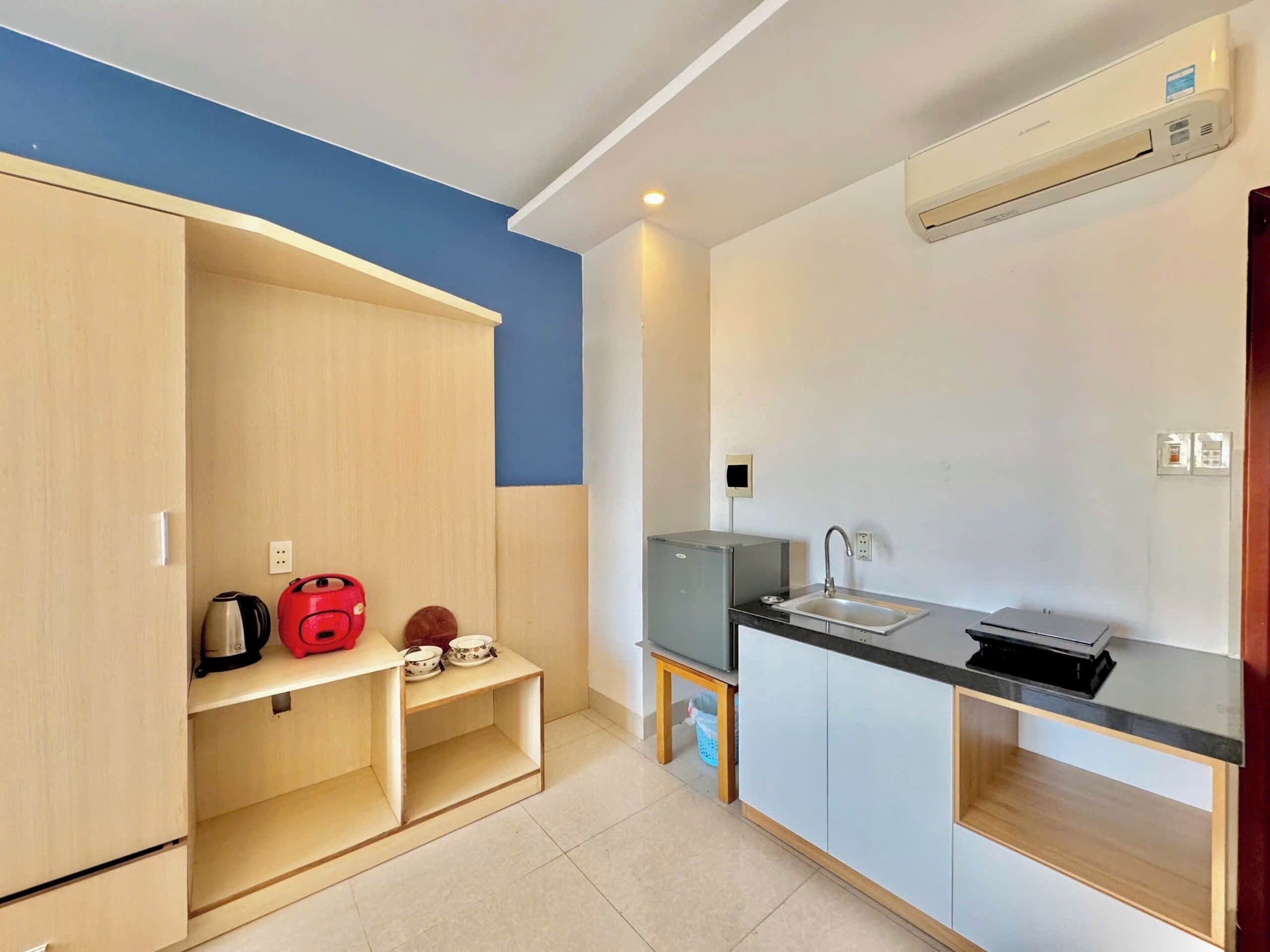 A compact kitchen with a built-in sink, a kettle, and a small refrigerator.