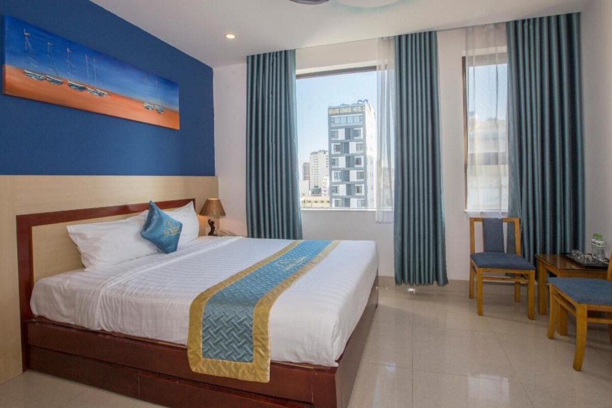 Quarto de hotel com cama, uma pintura, vista de edifícios e área de refeições.