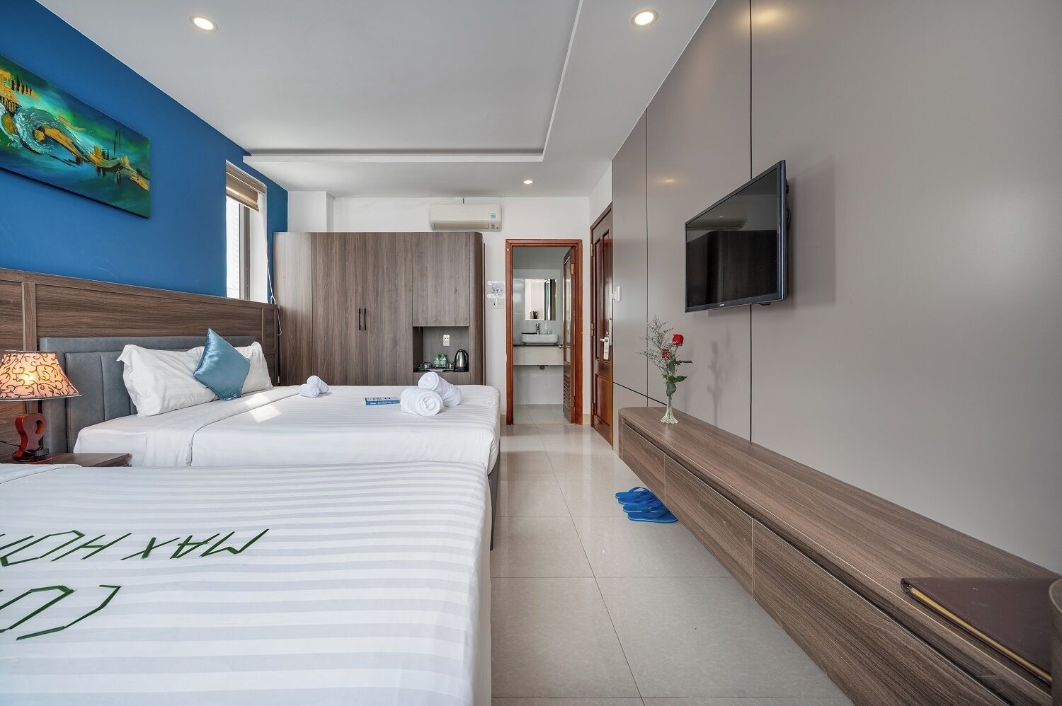 A modern hotel room with two beds, a TV, and a painting on the wall.
