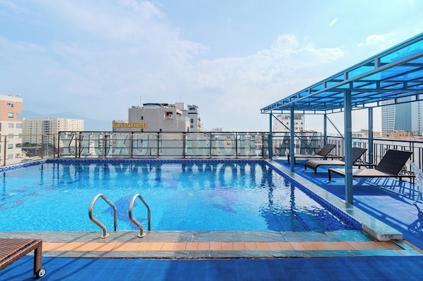 Una piscina en la azotea con dos escaleras metálicas, sillas de descanso y una zona cerrada con cristal.