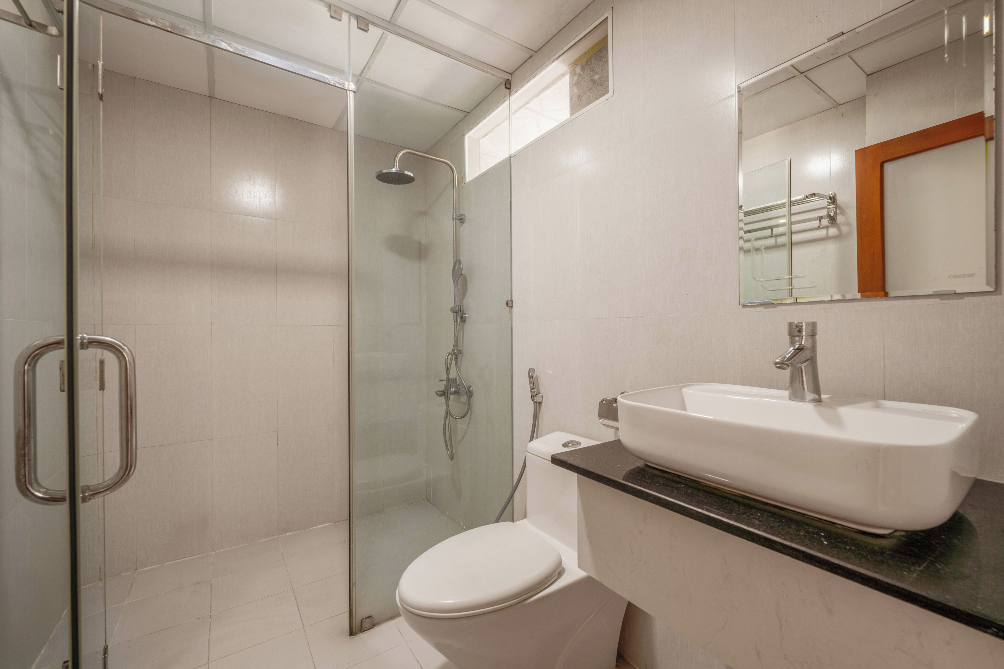A modern bathroom with a glass-enclosed shower, a white toilet, and a sink with a mirror above it.