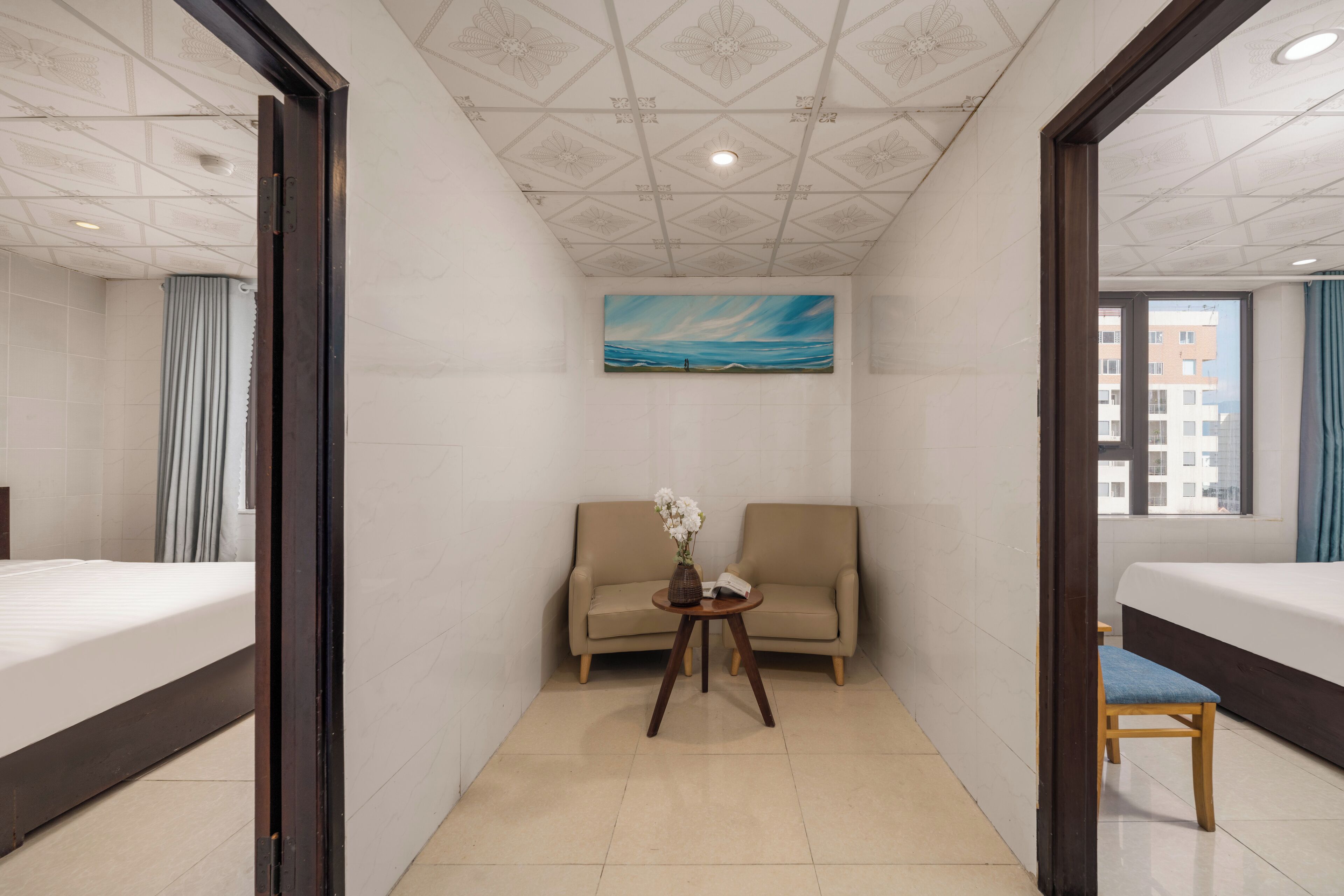 A hotel room with a bed, a sofa, a small table with a vase, and a painting of a seascape on the wall.