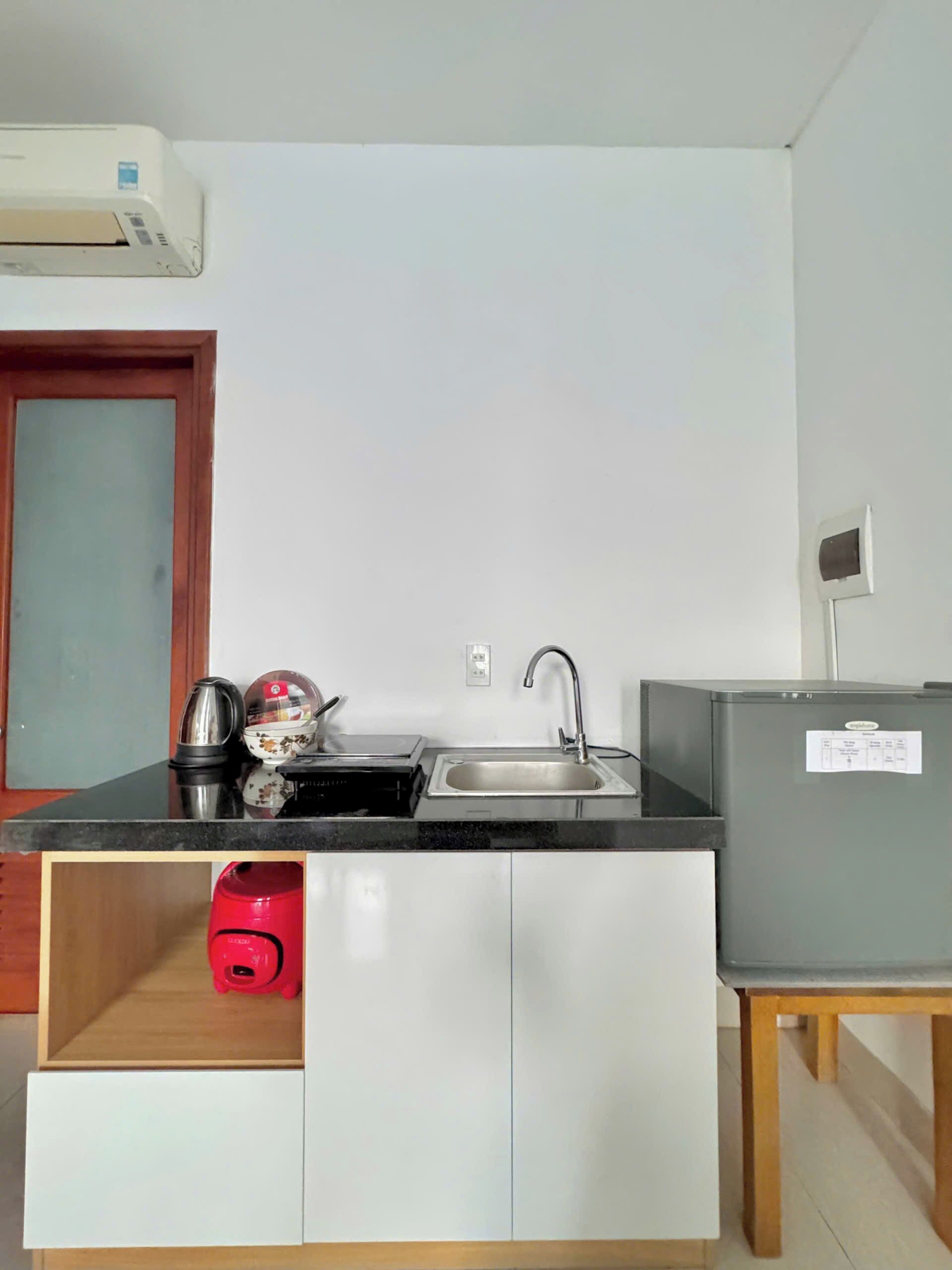 Una cocina con encimera negra, armarios blancos, un lavamanos de acero inoxidable, una tetera, un tostador y un refrigerador.
