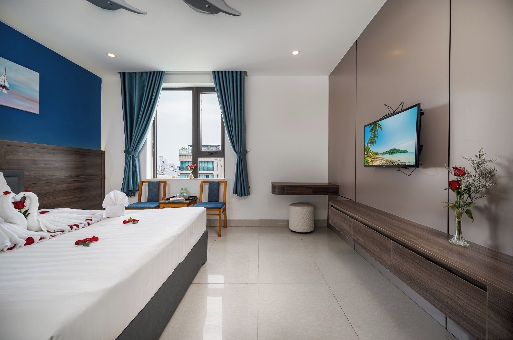 A modern hotel room with a large bed, a desk, a TV, and a view of the city.