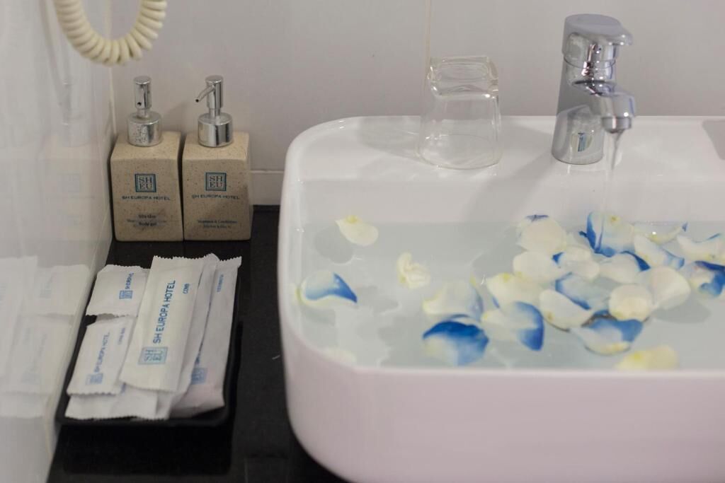 A bathroom sink with flower petals, toiletries, and a hand soap dispenser.