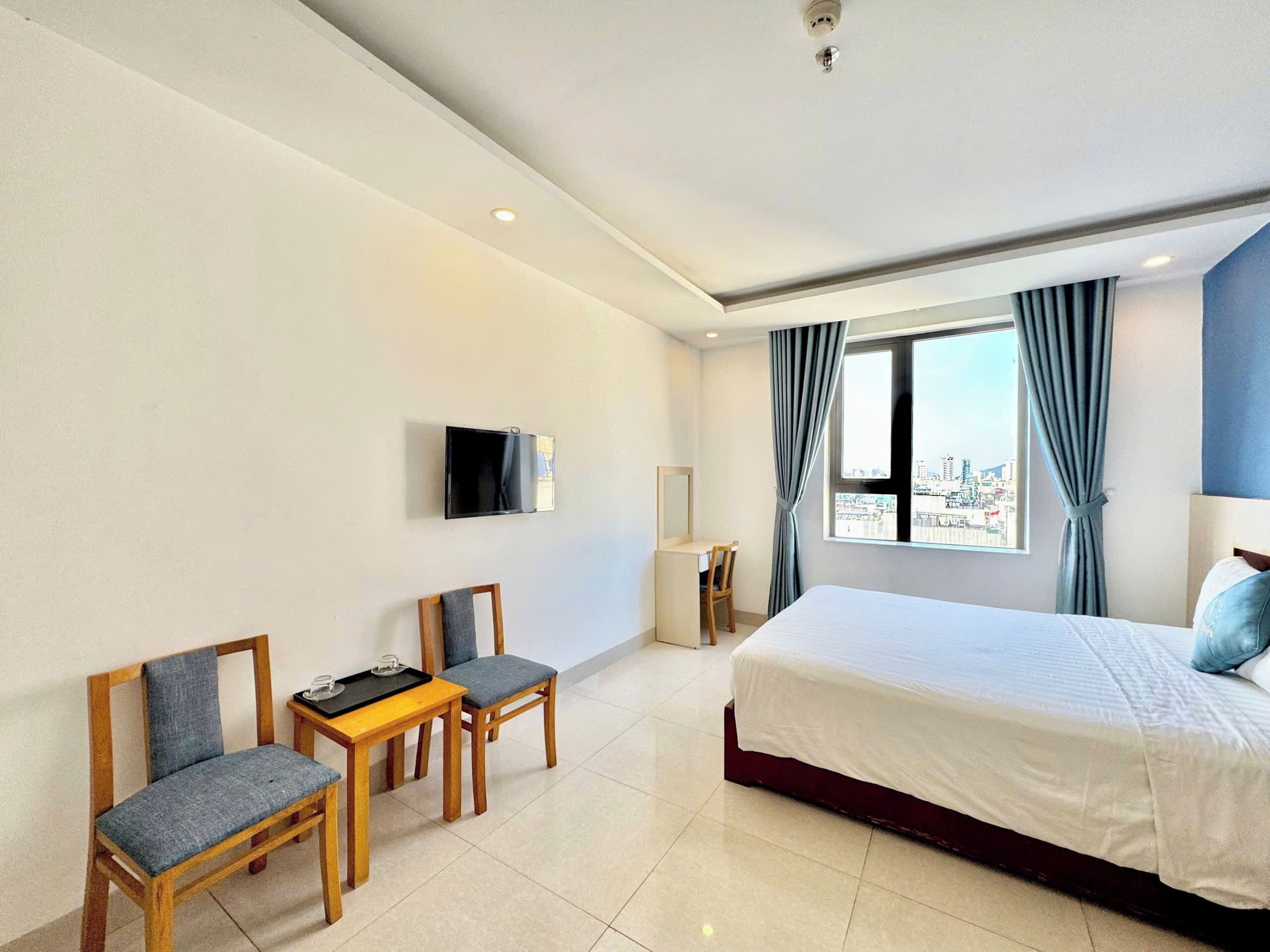 Habitación de hotel con cama, dos sillones, una mesita, televisor y ventana con cortinas.