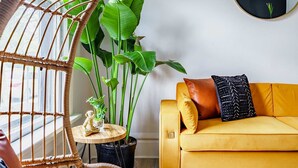 A room with a yellow sofa, a round mirror, a hanging chair, and a large green plant. - Short North & Downtown & OSU | Near High Street | Free Parking | 5,800+ Reviews (Columbus)