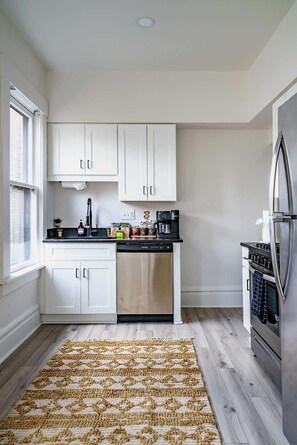 A modern kitchen with white cabinetry, a dishwasher, a coffee machine, and a stainless steel refrigerator. - Short North & Downtown & OSU | Near High Street | Free Parking | 5,800+ Reviews (Columbus)