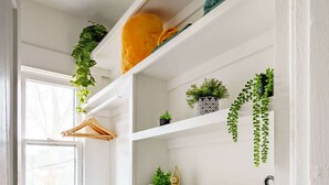 A white interior with a wooden floor, a hanging plant, a window, and a shelf with folded towels. - Short North & Downtown & OSU | Near High Street | Free Parking | 5,800+ Reviews (Columbus)