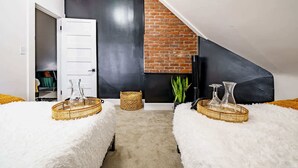 A modern loft bedroom with a sloped ceiling, exposed brick wall, and a white door leading to a closet. - Short North & Downtown & OSU | Near High Street | Free Parking | 5,800+ Reviews (Columbus)