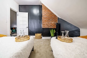Ein modernes Schlafzimmer im Loft-Stil mit schräg verlaufender Decke, freiliegender Backsteinwand und einer weißen Tür zu einem Kleiderschrank.