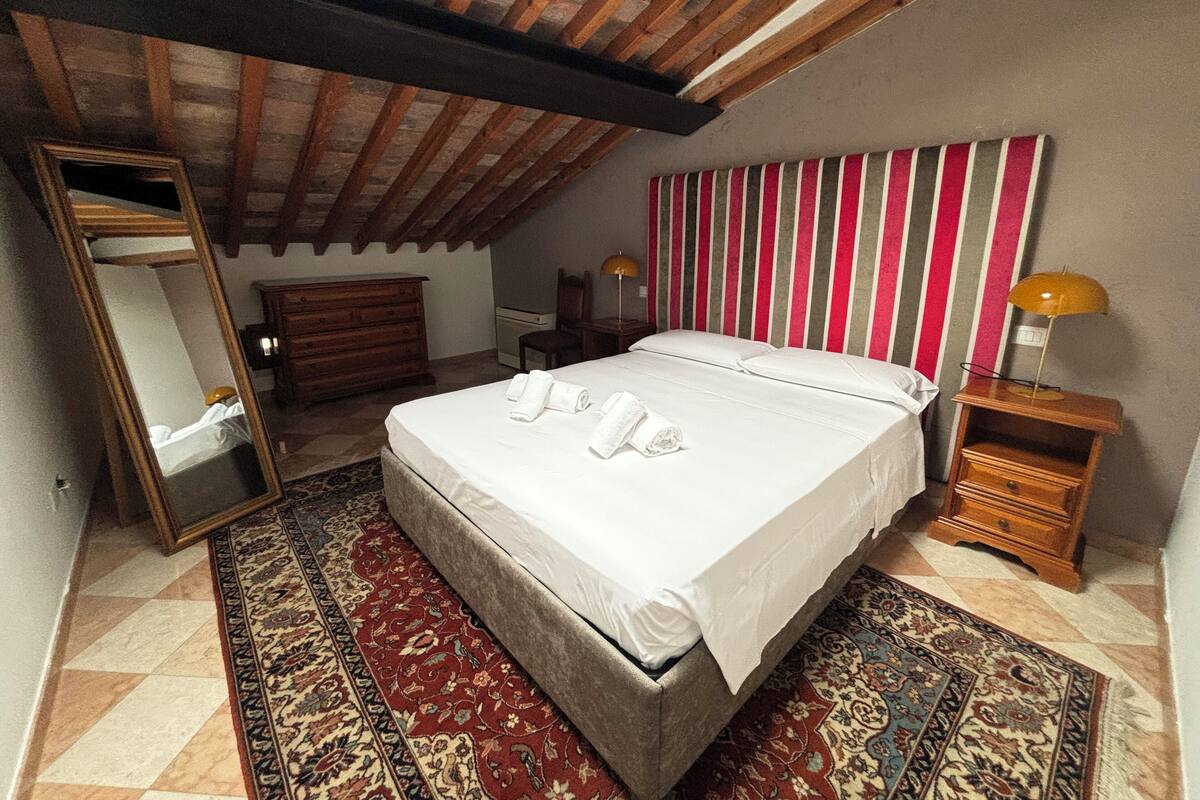 Une chambre avec un grand lit, un plafond en bois, un mur à rayures, un miroir, une table de chevet et un tapis à motifs.