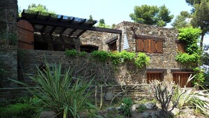 Ein Steingebäude mit Holzläden, einer Pergola und einem Garten mit Kakteen.