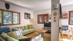 Ein Wohnzimmer mit einem grünen Sofa, einem Couchtisch, einem Fernseher und einem Fenster mit Jalousien.