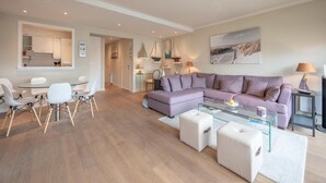A modern living room with a glass coffee table, a purple sofa, and a dining area with white chairs. - Apartment in Duinbergen Near Sailing School (Knokke-Heist)