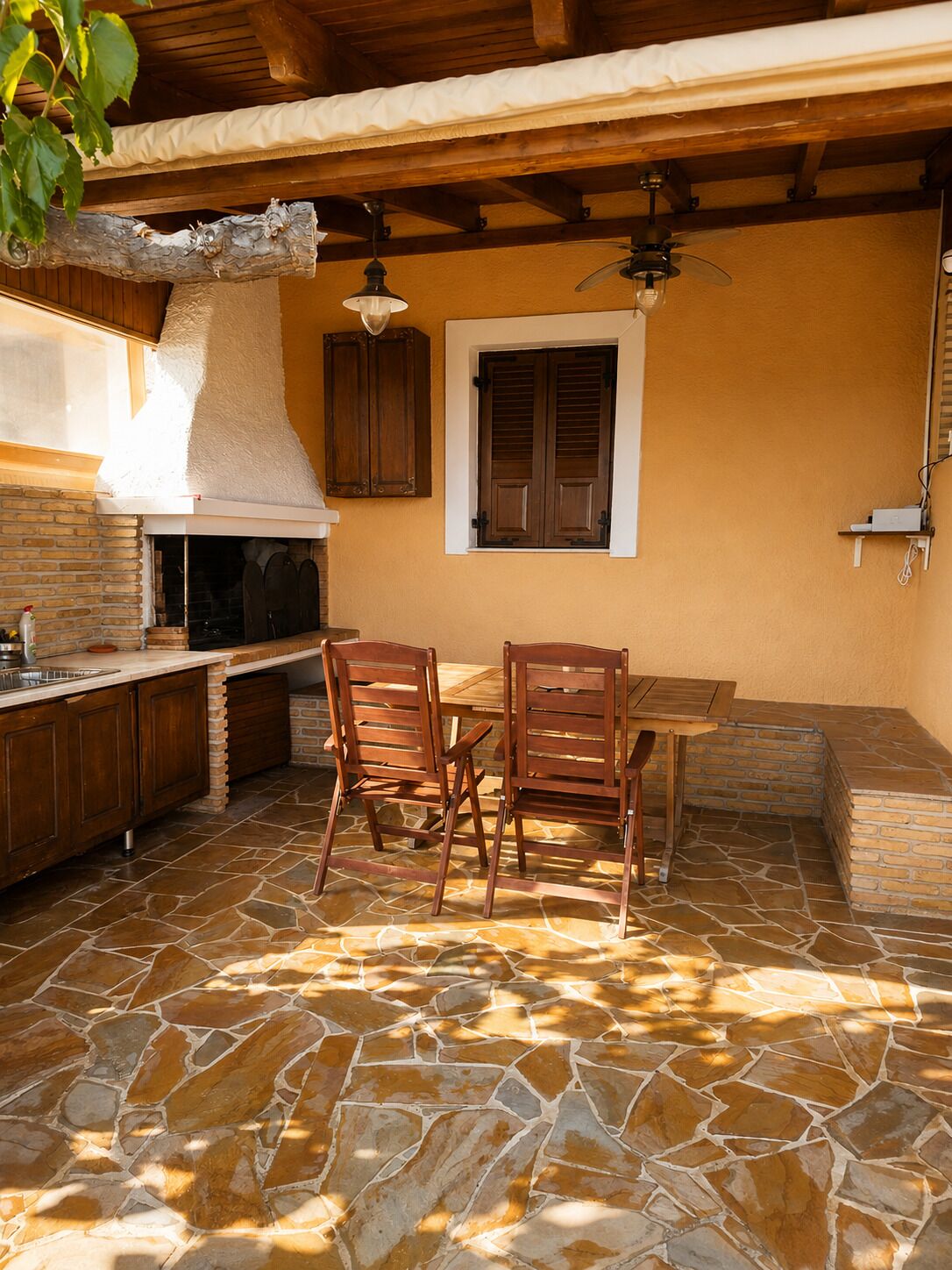 Un área de cocina al aire libre con suelo de piedra, mobiliario de madera y un horno de ladrillo.